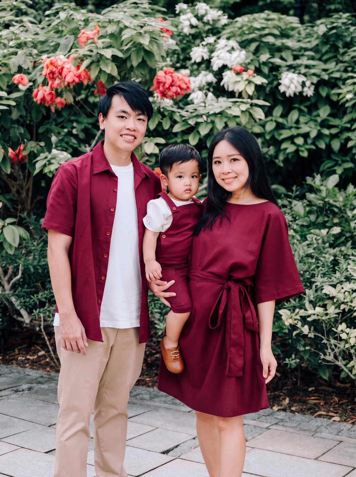 A family of three wearing matching burgundy linen shirt, dungaree and dress.