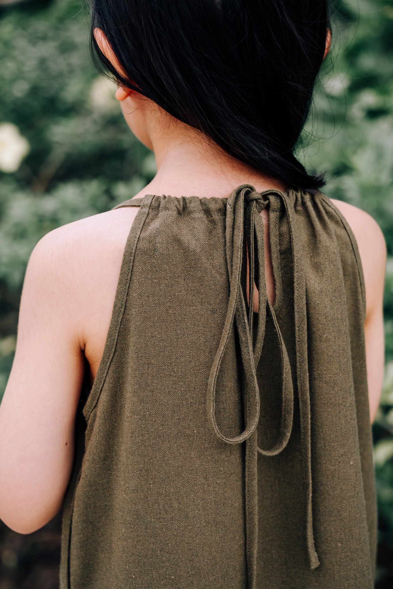 Close up of back of young girl wearing MOSS Mini Isla Dress in soft moss green linen blend fabric