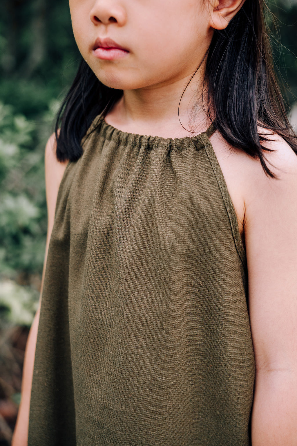 Close up of young girl wearing MOSS Mini Isla Dress in soft moss green linen blend fabric