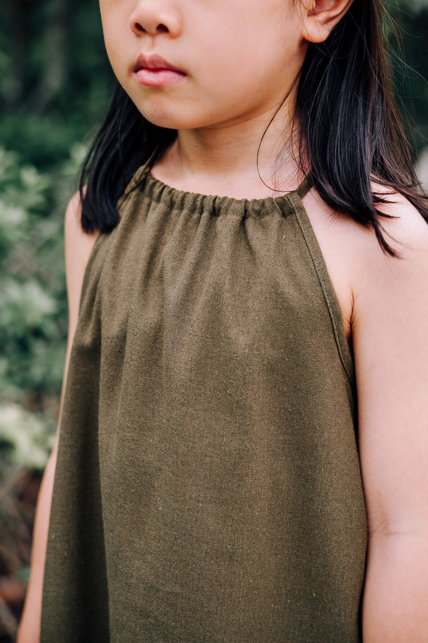 Close up of young girl wearing MOSS Mini Isla Dress in soft moss green linen blend fabric