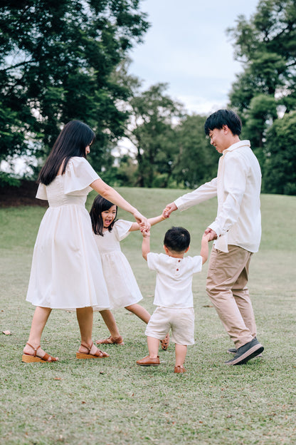 Family wearing SAND Collection matching linen outfits: mother in Mira A-Line Dress, father in Elio Linen Shirt, daughter in Mini Mira Dress, toddler in Mini Noa Linen T-Shirt