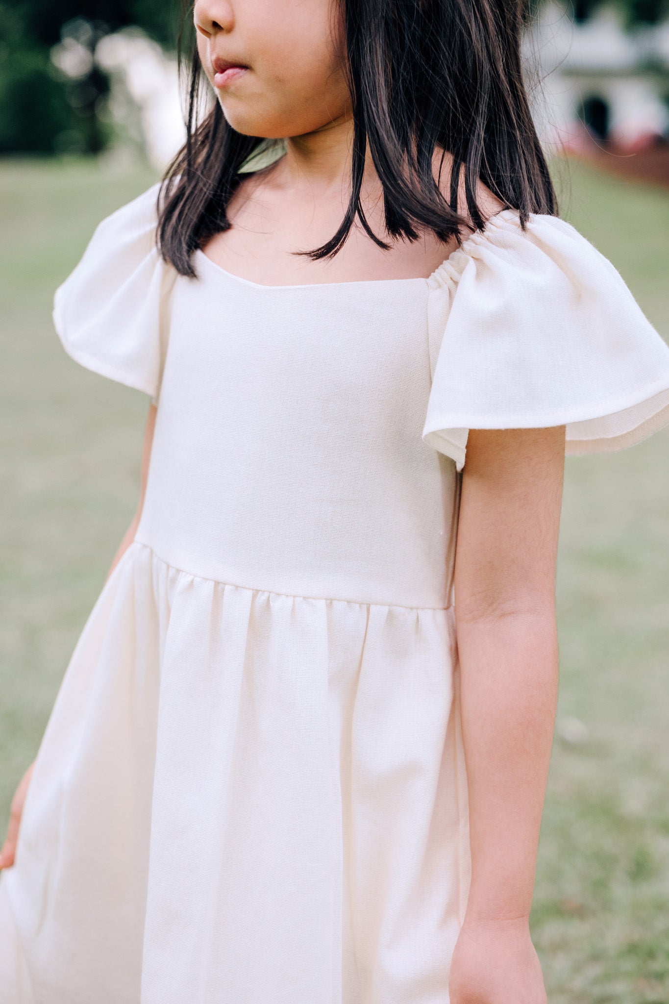 Close up of child wearing SAND Mini Mira Dress in soft sand linen blend