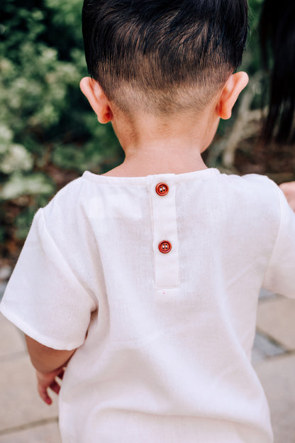 Back view of child wearing SAND Mini Noa T-Shirt in neutral tone sand linen blend fabric with faux wooden buttons