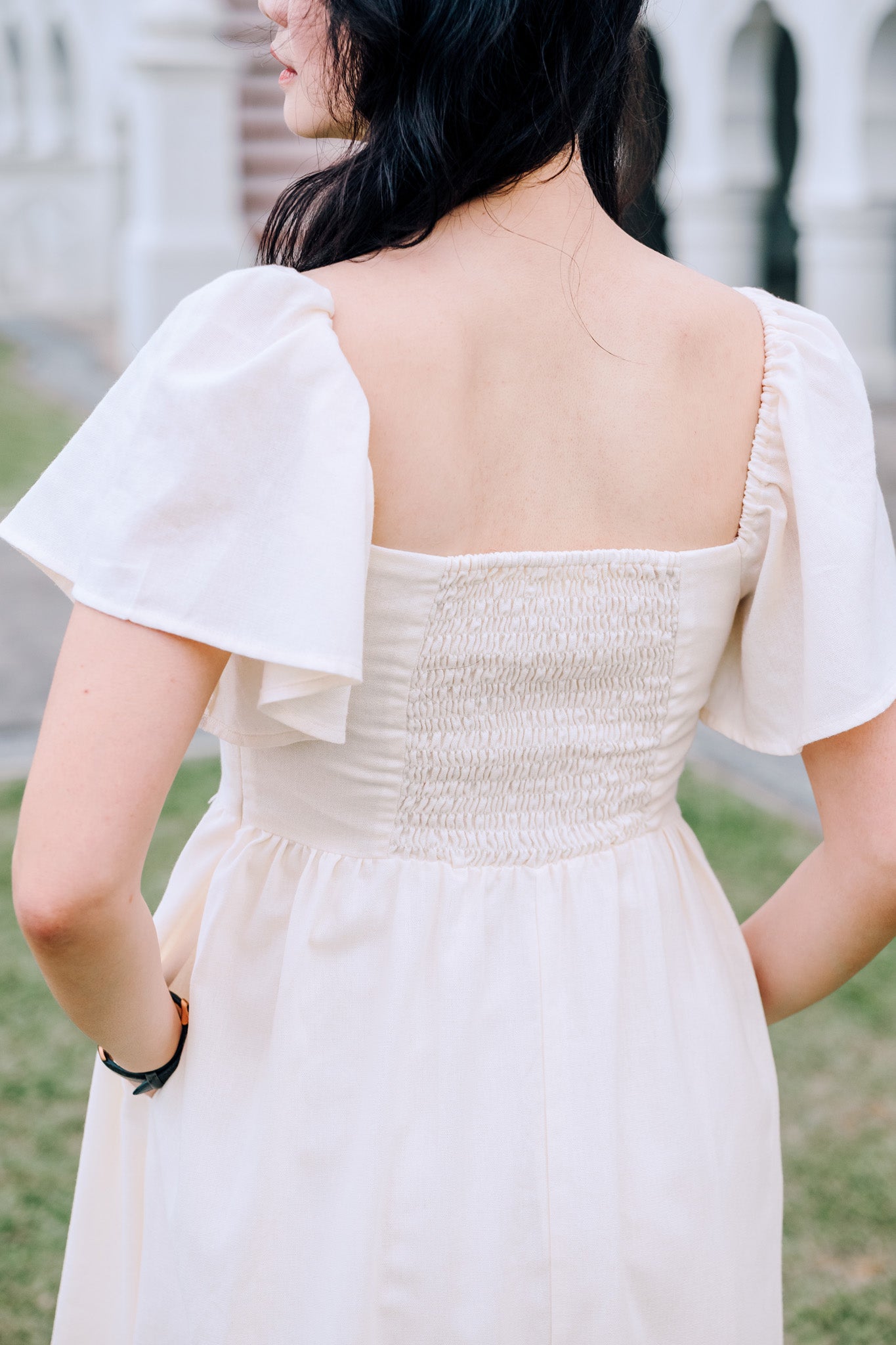 Close-up of back view of SAND Mira A-Line Dress smocked back and ruffle sleeves in sand