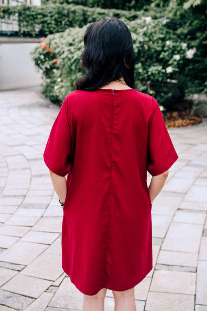 Back view of woman wearing a knee length burgundy linen dress standing on a paved walkway