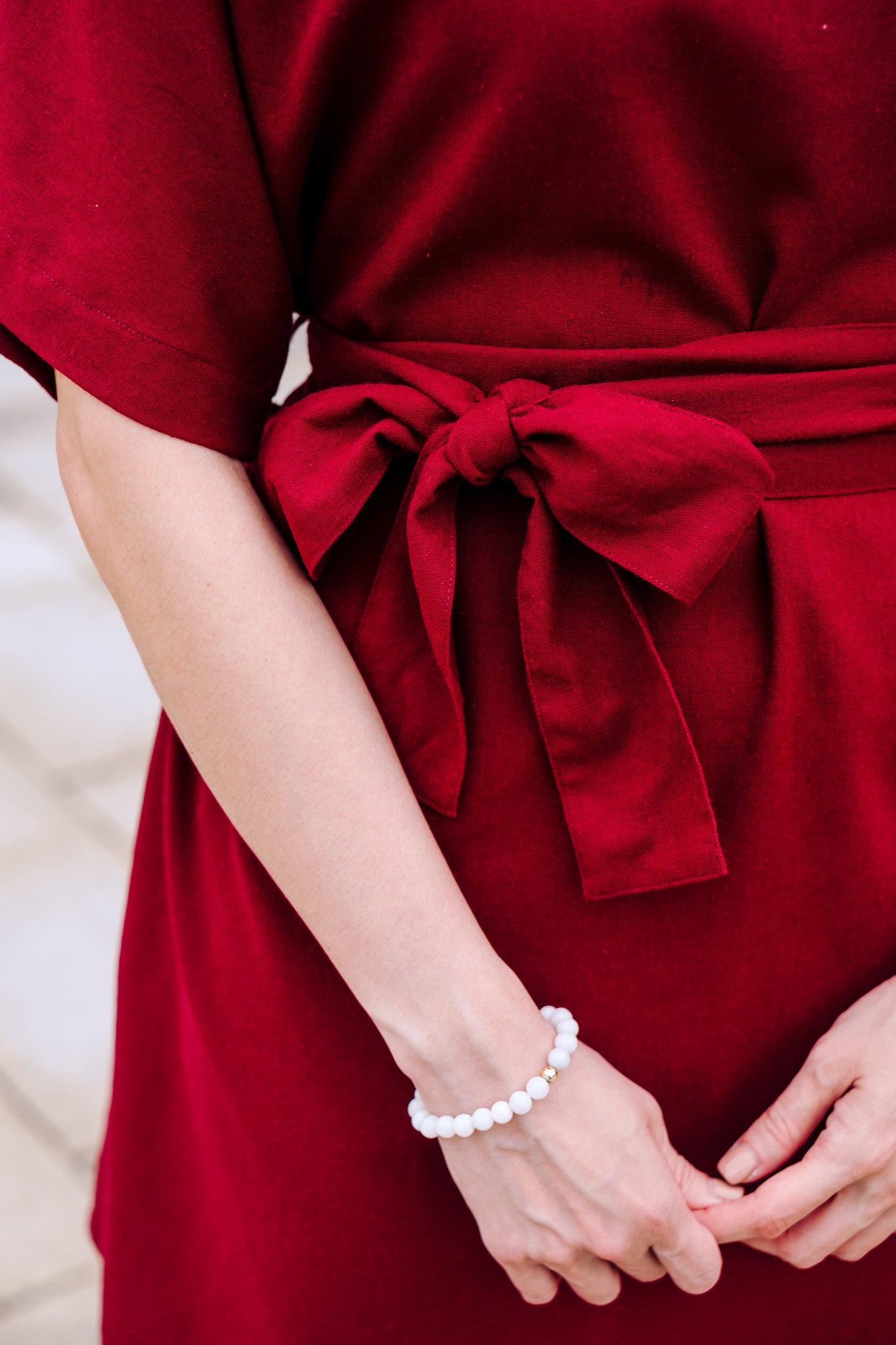 Burgundy linen dress with a bow detail on a neutral background