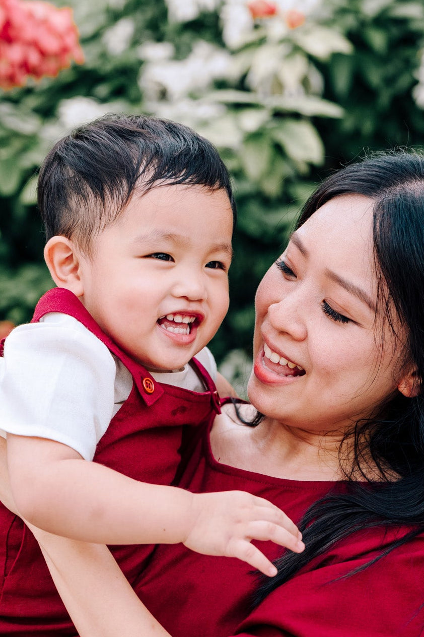 Woman in a burgundy linen dress holding a child in matching linen dungaree