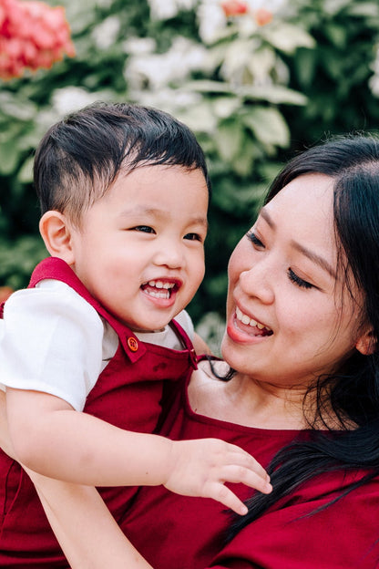Woman in a burgundy linen dress holding a child in matching linen dungaree