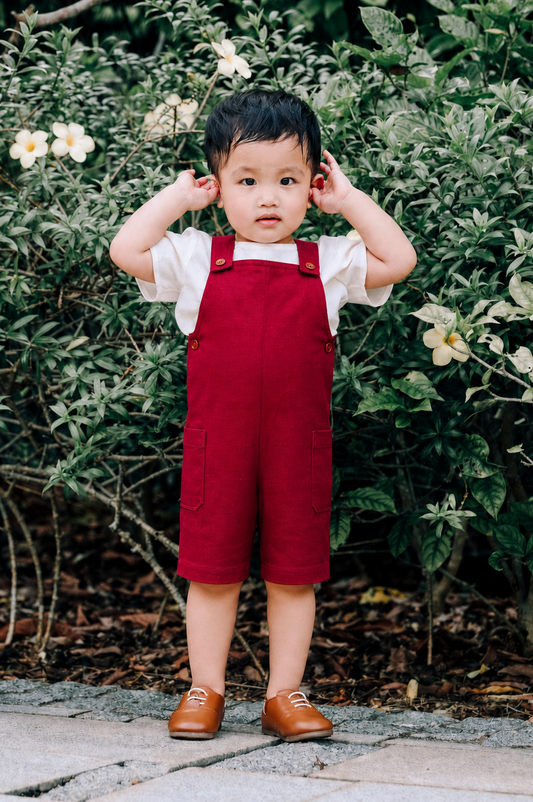 Boy wearing burgundy linen dungaree and with warm sand linen tee.